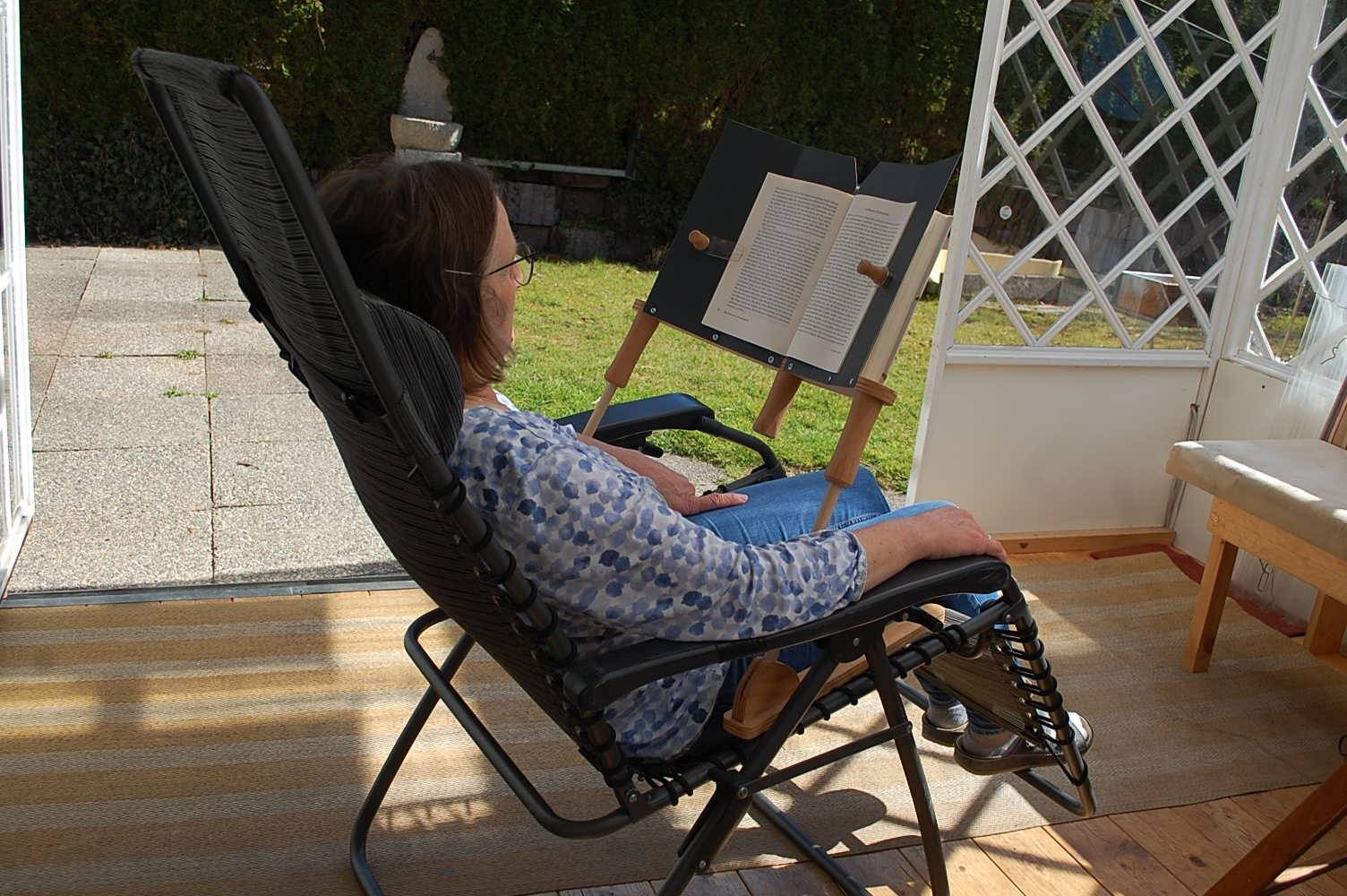 Frau liest im Sitzen auf einem Liegestuhl im Garten mit dem BookBock Lesegestell – bequemes Lesen draußen