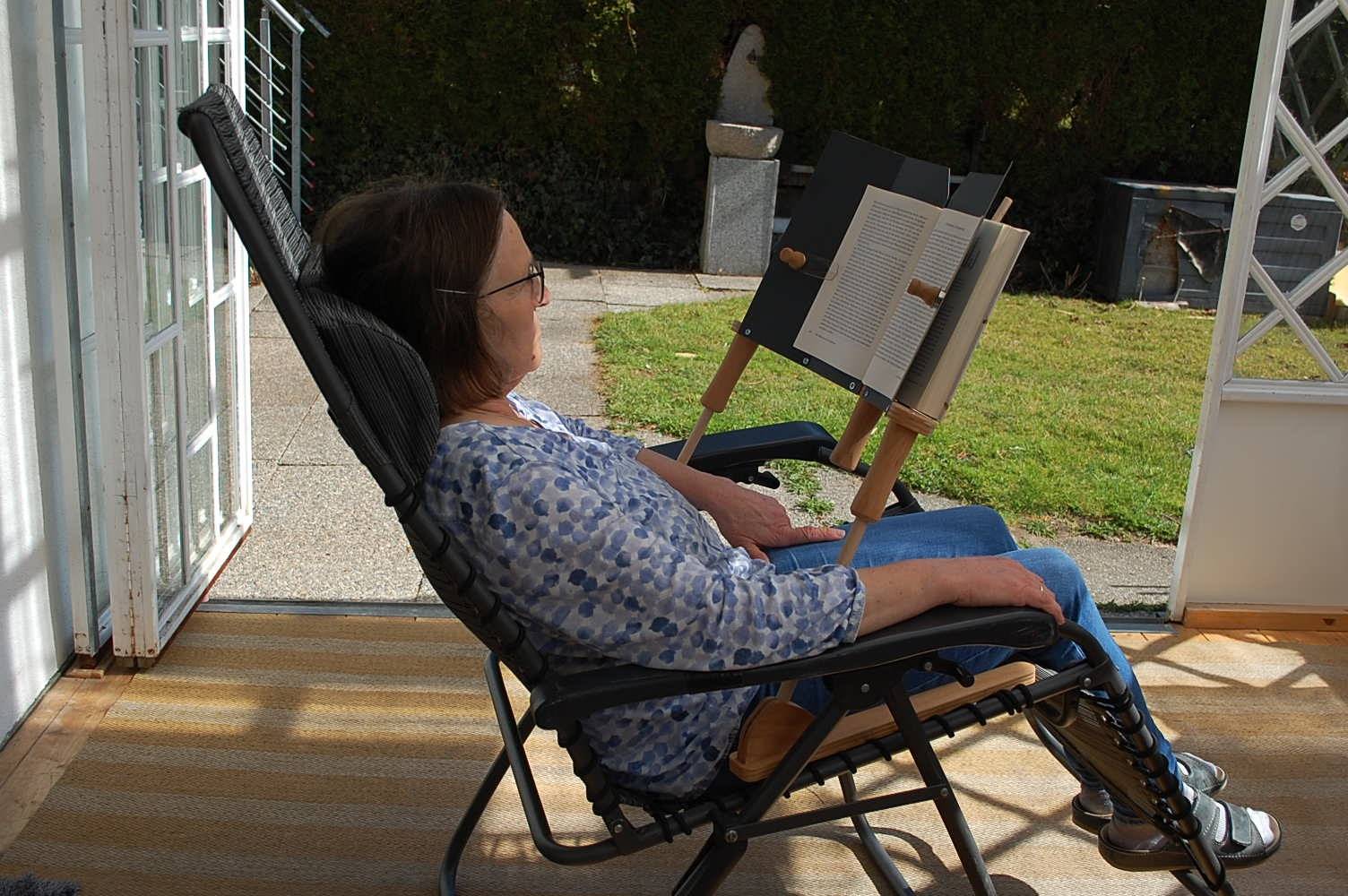 Frau nutzt den BookBock Buchständer im aufrechten Sitzen auf der Terrasse – entspanntes Lesen ohne die Arme zu belasten