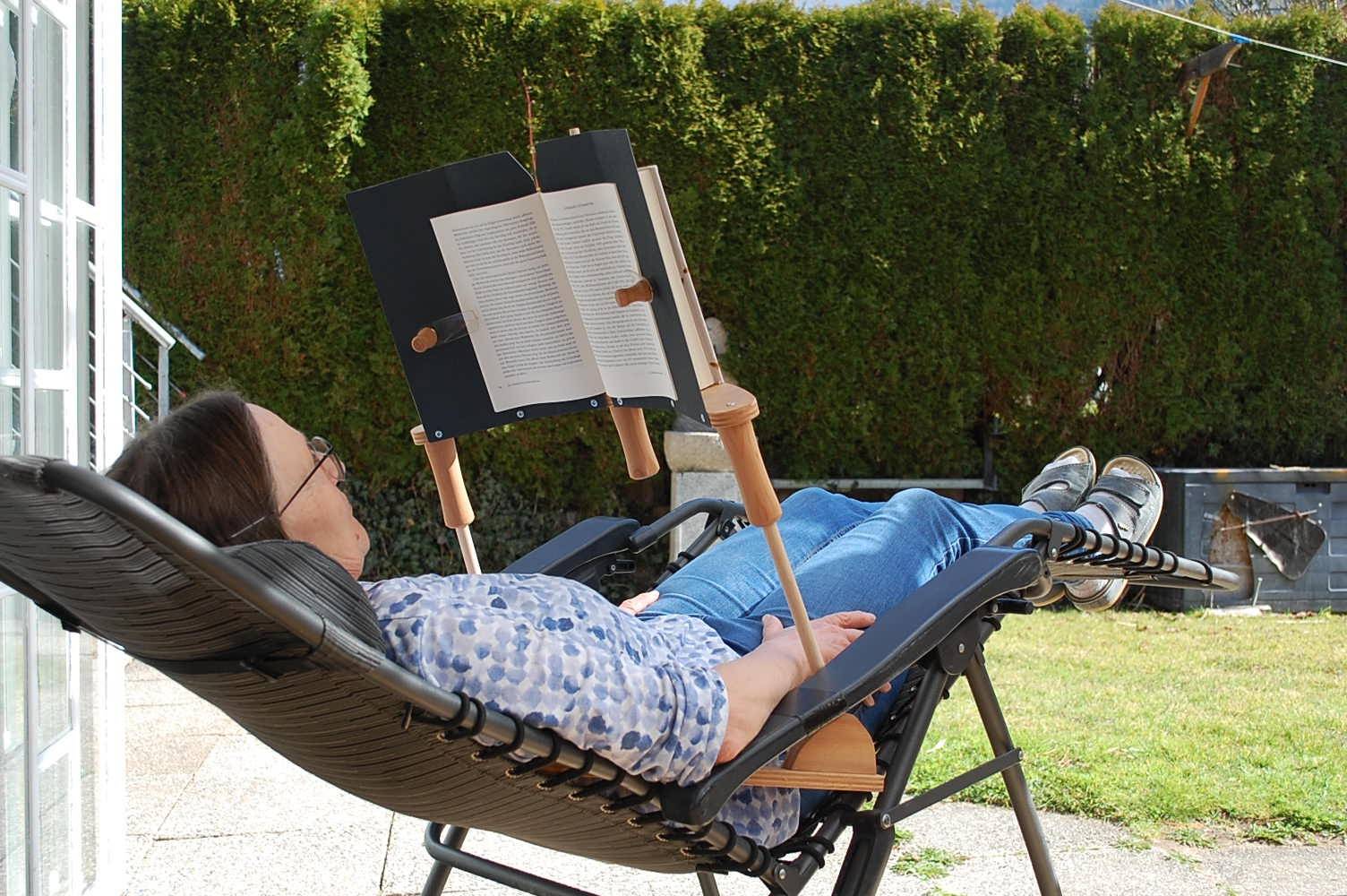 Frau liest zurückgelehnt im Liegestuhl draußen mit dem BookBock Lesegestell – Buchständer für jede Sitzposition