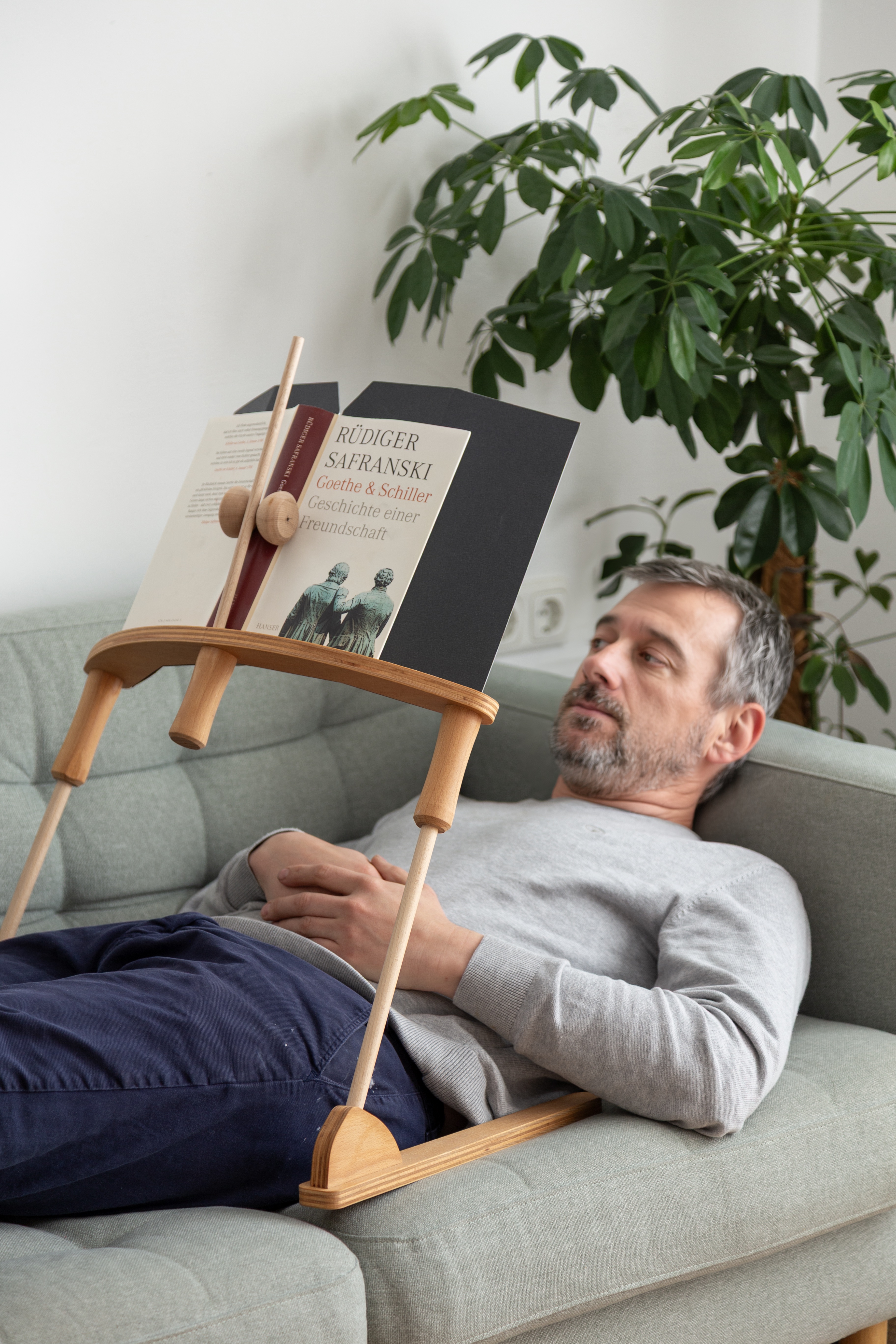 Mann liest entspannt im Liegen auf dem Sofa mit dem BookBock Lesegestell – ergonomischer Buchständer für jede Position