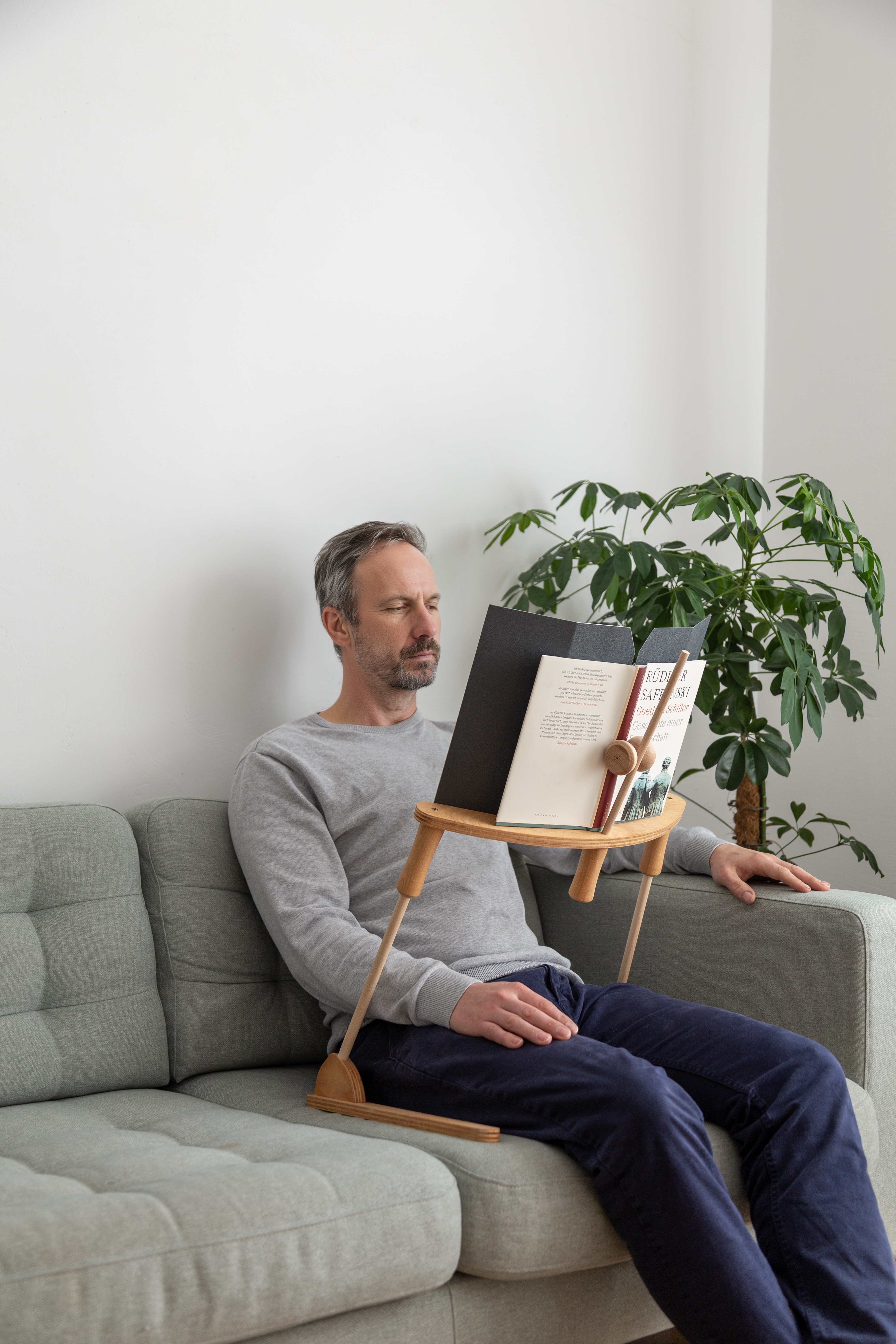 Mann liest bequem im Sitzen auf dem Sofa mit dem BookBock Lesegestell – freihändiges Lesen ohne Arme zu belasten